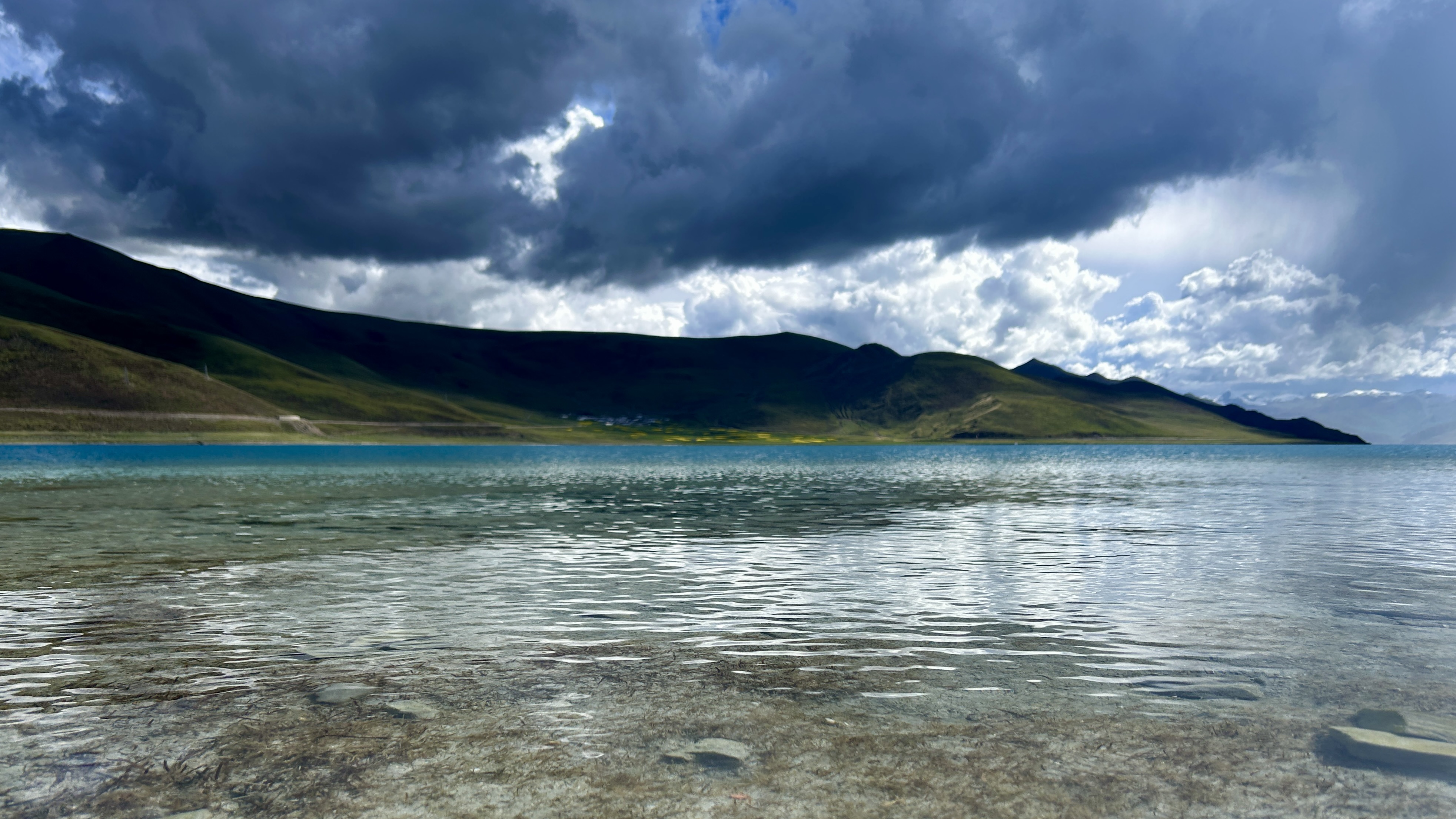A mountain lake beneath storm clouds with bright openings in the sky.