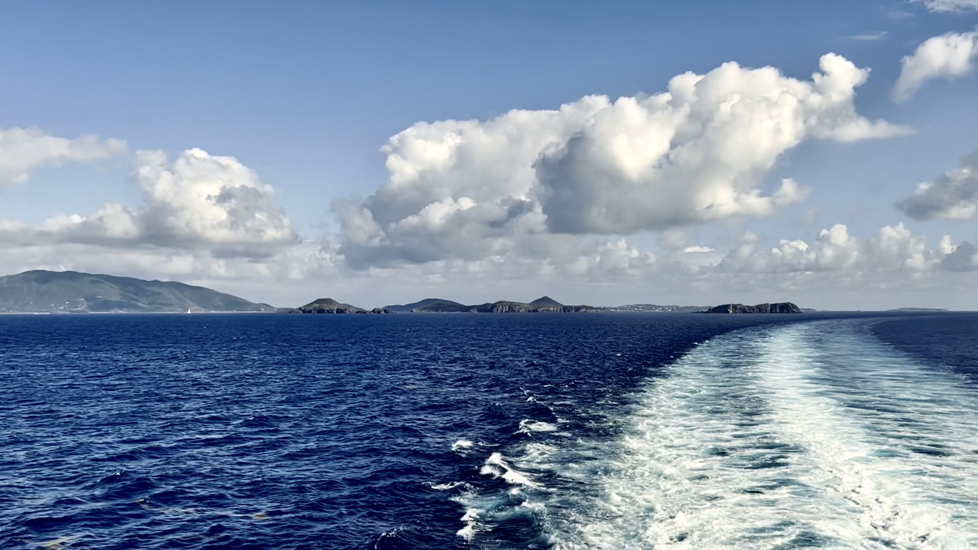 Ocean wake trailing toward distant islands under bright clouds